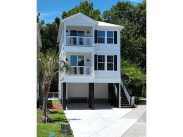 Two-story stilt home featuring balconies, dark shutters, and a concrete driveway and stairs at 52 Fish Shack Alley, Murrells Inlet, SC 29576