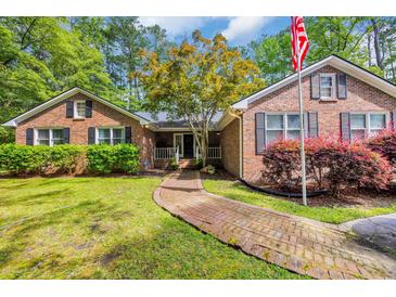 Charming brick home featuring a brick walkway, mature trees, lush landscaping, and a welcoming American flag at 196 John Waites Ct., Georgetown, SC 29440