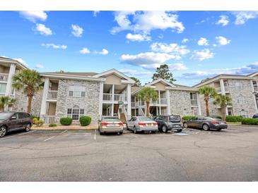 Condo building featuring stone facade, balconies, palm trees and ample parking on a sunny day at 4767 Wild Iris Dr. # 203, Myrtle Beach, SC 29579