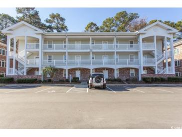 Three-story condo building with exterior stairs, white railings, and ample parking in a landscaped community at 690 Riverwalk Dr. # 201, Myrtle Beach, SC 29579