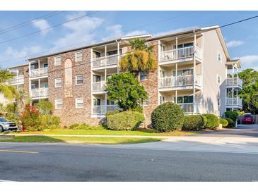 Three-story condo building featuring a brick facade and multiple balconies with white railings and mature landscaping at 1212 Ocean Blvd. S # 202, Surfside Beach, SC 29575