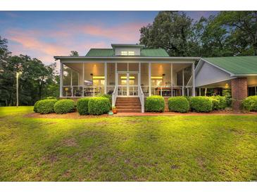 Inviting home featuring a spacious screened porch, beautiful landscaping, and warm lighting at dusk at 3231 Center Rd., Georgetown, SC 29440