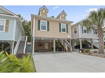 Charming raised beach home with tan siding, green shutters, and covered parking, surrounded by lush landscaping at 4331 Grande Harbour Blvd., Little River, SC 29566