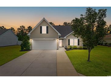 Charming home featuring a two-car garage, manicured lawn, and beautiful landscaping at dusk at 620 Seth Ln., Longs, SC 29568