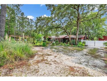 Ranch-style home featuring a cozy yard and a large, gravel driveway surrounded by mature trees and natural foliage at 5114 Cowart Ct., Murrells Inlet, SC 29576
