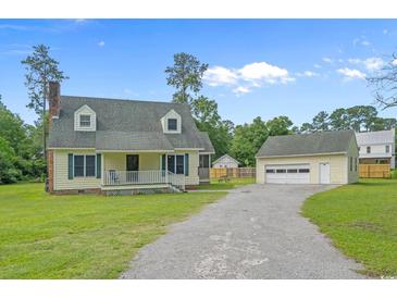 Charming two-story home with yellow siding, a white porch, and a detached garage on a large lot at 124 Wicklow Way, Pawleys Island, SC 29585