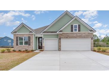 Charming home featuring a two-car garage, brick accents, and light green siding beneath a blue sky at 7175 Shooting Star Way, Myrtle Beach, SC 29579