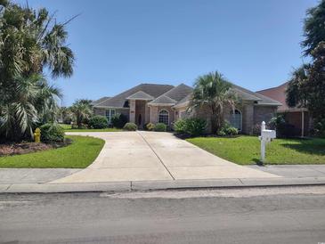 Charming brick home featuring a circular driveway and mature landscaping, including palm trees, on a sunny day at 413 Sea Vista Ln., North Myrtle Beach, SC 29582