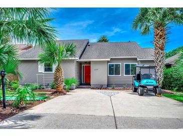 Charming home featuring a vibrant red door, palm trees, manicured landscaping, and a golf cart parked in the driveway at 10056 Kings Rd., Myrtle Beach, SC 29572