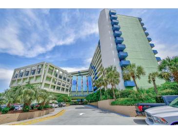 Exterior of the Coral Beach Resort featuring a parking area, palm trees, and blue accents against a cloudy sky at 1105 S Ocean Blvd. # 330, Myrtle Beach, SC 29577
