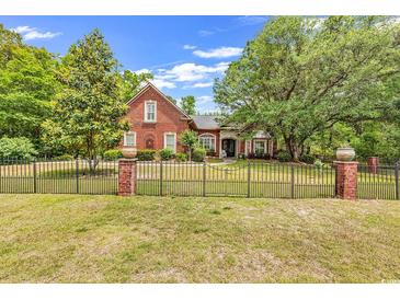 Charming red brick home with manicured front lawn, gated entry, and lush trees providing shade at 487 Trestle Way, Conway, SC 29526