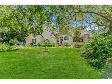 Beautiful yellow home featuring a well-manicured lawn, mature trees, and a charming front yard firepit at 189 Aspen Loop, Pawleys Island, SC 29585
