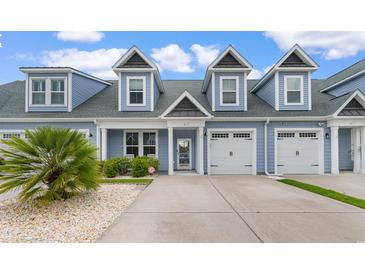 Charming blue two-story townhouse featuring a well-manicured lawn and attached garages under a bright blue sky at 413 Goldenrod Circle # 2B, Little River, SC 29566