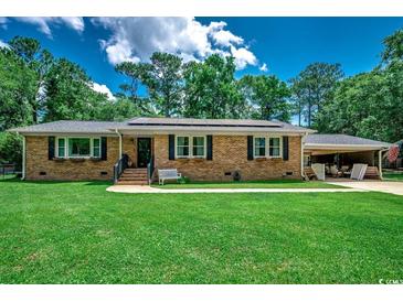 Charming brick home featuring manicured front lawn, solar panels, and covered carport at 4189 Schoolhouse Circle, Little River, SC 29566