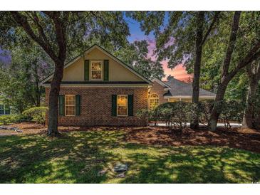 Charming brick home with green shutters nestled among mature trees in a lush, green lawn at 90 Old Carriage Ln., Pawleys Island, SC 29585