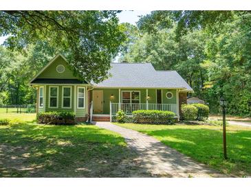 Charming green home featuring a welcoming front porch and well-manicured lawn and landscaping at 309 Otter Run Rd., Pawleys Island, SC 29585