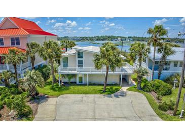 Inviting two-story home with a white exterior, waterfront views, a manicured lawn, and palm trees at 624 Dogwood Dr. S, Garden City Beach, SC 29576