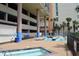 Outdoor pool and spa area, featuring lounge chairs, tropical landscaping, and a parking garage at 501 S Ocean Blvd. # 1104, North Myrtle Beach, SC 29582