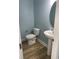 A powder room with a pedestal sink, a round mirror, and a toilet against blue walls and modern floors at 1738 Cenith Dr., North Myrtle Beach, SC 29582