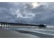 View of a rustic wooden fishing pier extending into the ocean under a cloudy sky at 405 White Willow Way, Longs, SC 29568