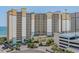 Exterior shot of large condo building with multiple balconies, palm trees, and a parking garage near the beach at 4800 S Ocean Blvd. # 1219, North Myrtle Beach, SC 29582