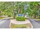 Welcoming community entrance with lush greenery, a decorative sign, and paved roads at 1900 Shell Ct., Surfside Beach, SC 29575