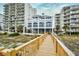 Exterior daytime view of a boardwalk leading to a condo building complex surrounded by manicured lawns and palm trees at 6244 Catalina Dr. # 4603, North Myrtle Beach, SC 29582