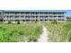 Sandy beach path with native grass leading up to condo building with balconies in background at 4406 N Ocean Blvd. # A-1, North Myrtle Beach, SC 29582