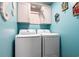 Modern laundry room featuring side-by-side washer and dryer units with overhead cabinets and a bright blue accent wall at 1031 N Dogwood Dr., Surfside Beach, SC 29575