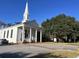 An all white traditional church with white pillars, a tall steeple and a small parking lot at 3127 Tiger Tail Rd., Conway, SC 29526