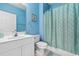 Bright blue bathroom featuring a white vanity, toilet, and a shower with a patterned curtain at 5751 Oyster Catcher Dr. # 633, North Myrtle Beach, SC 29582