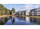 Exterior view of white condos with screened porches reflecting in a tranquil pond under a partly cloudy sky at 5060 Windsor Green Way # 304, Myrtle Beach, SC 29579