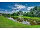 Scenic pond surrounded by lush green grass and mature trees under a bright, partly cloudy sky at 583 Meadowgrass Ct., Myrtle Beach, SC 29588