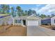 Quaint home featuring light green siding and a white garage door, complemented by lush, tall trees in the background at 609 Gryffindor Dr., Longs, SC 29568