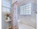 Modern shower with bench and clear glass block window featuring floral curtains and white tiled walls at 920 Leather Leaf Ln., Longs, SC 29568