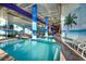 A well-lit indoor pool features clear waters and views of colorful waterslides, surrounded by lounge chairs, palm trees and murals at 5200 N Ocean Blvd. # 155, Myrtle Beach, SC 29577