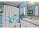 Blue bathroom with floral shower curtain, granite countertop, and storage cabinet at 6001-L11 South Kings Hwy., Myrtle Beach, SC 29575