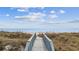 Elevated boardwalk over dunes leading to a sandy beach and the ocean under a cloudy sky at 817 S Ocean Blvd. # 105, North Myrtle Beach, SC 29582