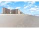 Expansive sandy beachfront view of high-rise condos under bright blue skies with scattered clouds at 100 North Beach Blvd. # 506, North Myrtle Beach, SC 29582