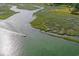 Aerial view of a boat cruising along the glistening waterway with lush greenery on the banks and golf course nearby at 118 Ellington Ln., Pawleys Island, SC 29585