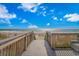 Wooden boardwalk leading down to a sandy beach and ocean under a bright blue sky with fluffy clouds at 504 N Ocean Blvd. # 310, Myrtle Beach, SC 29577