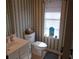 Bathroom with white sink and toilet, paired with decoratively-striped wallpaper and a sunny window at 3158 River Bluff Ln., Little River, SC 29566