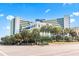 Bright and airy exterior view of a modern beachfront resort with lush palm trees and manicured landscaping at 1105 S Ocean Blvd. # 604, Myrtle Beach, SC 29577