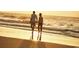 Romantic beach stroll: Couple walking hand-in-hand on the golden sand during a serene sunset at 2017 Lone Cypress Dr, Myrtle Beach, SC 29579