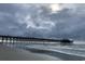 Wide ocean pier view stretching into the sea, featuring blue umbrellas against a cloudy sky and gentle waves at 990 Oak Hollow St., Longs, SC 29568