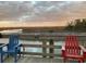 Relaxing waterfront view with Adirondack chairs overlooking a tranquil body of water and distant shoreline at sunset at 990 Oak Hollow St., Longs, SC 29568