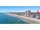 Wide beachfront view of an oceanfront tower, beach, and hotels with the treeline of a neighborhood visible at 1000 N Waccamaw Dr. # 205, Murrells Inlet, SC 29576