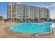Resort style pool with palm trees and blue umbrellas for relaxing near the community buildings at 5750 Oyster Catcher Dr. # 522, North Myrtle Beach, SC 29582