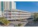 Exterior view of condo building with multiple floors, white railings, parking underneath, and a view of a high-rise building at 210 North Ocean Blvd. # 330, North Myrtle Beach, SC 29582