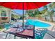 Inviting outdoor dining area with a colorful table setting, a vibrant red umbrella, and a view of the refreshing pool at 7609 Driftwood Dr., Myrtle Beach, SC 29572